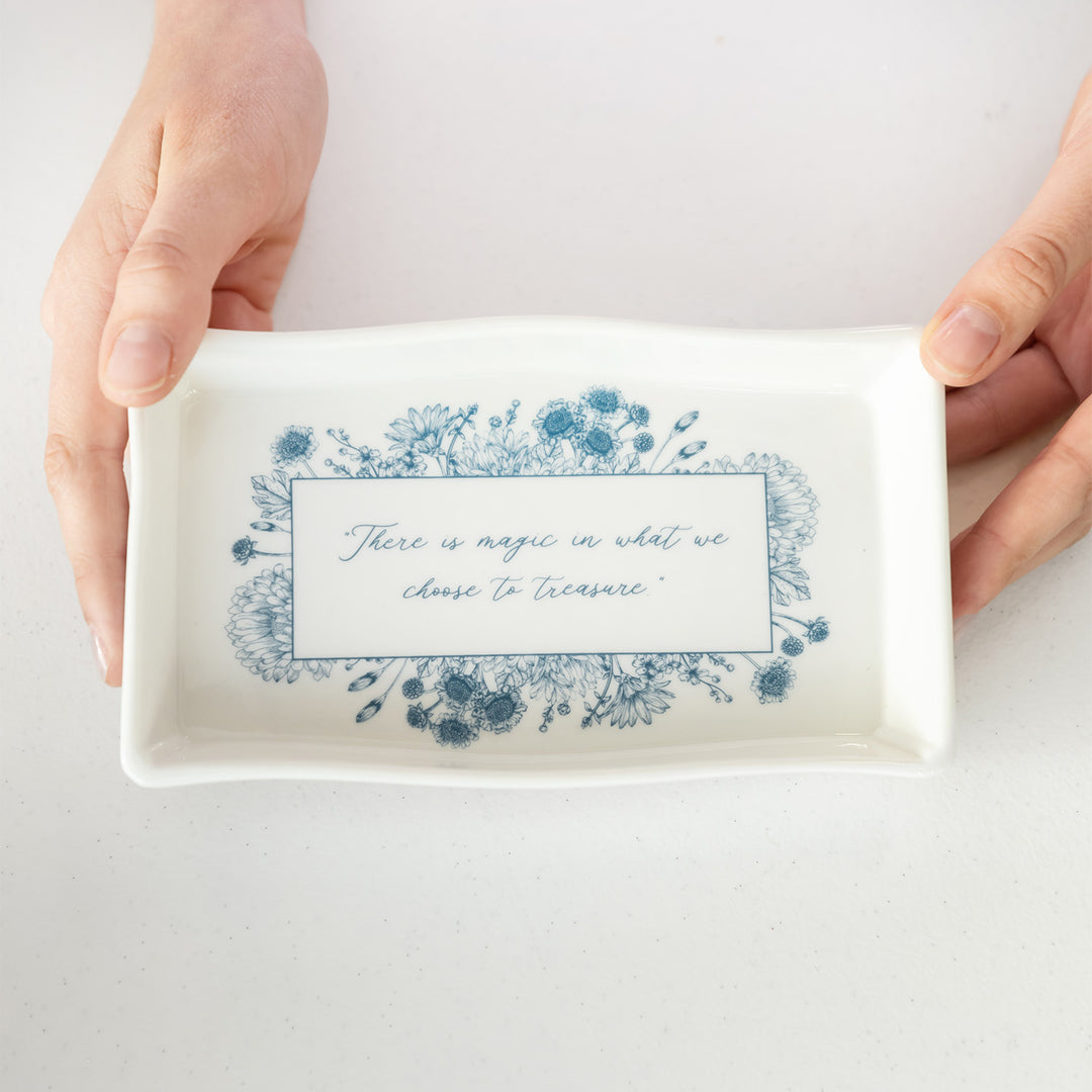 A ceramic trinket dish featuring blue floral pattern and a quote "There is magic in what we choose to treasure."