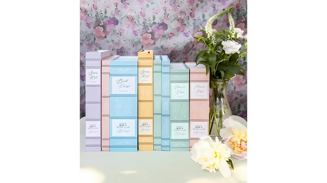 Colorful stack of 'Once Upon a Book Club' book boxes arranged on a table with a vase of flowers, set against a floral patterned background.