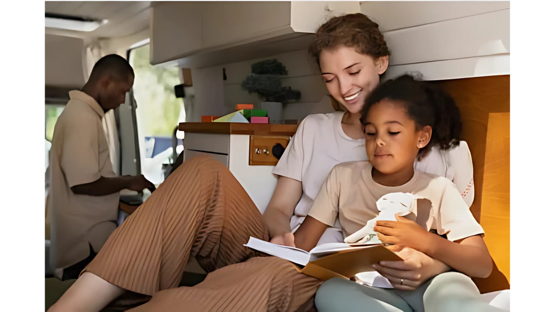 A mother and daughter sit together reading a book in a cozy space, while a man prepares food in the background, creating a warm atmosphere.