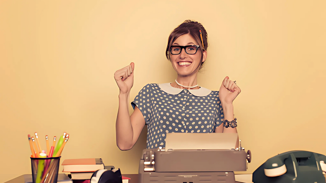 A cheerful woman with glasses and a vintage polka-dot dress sits at a desk with a typewriter, celebrating with raised hands.