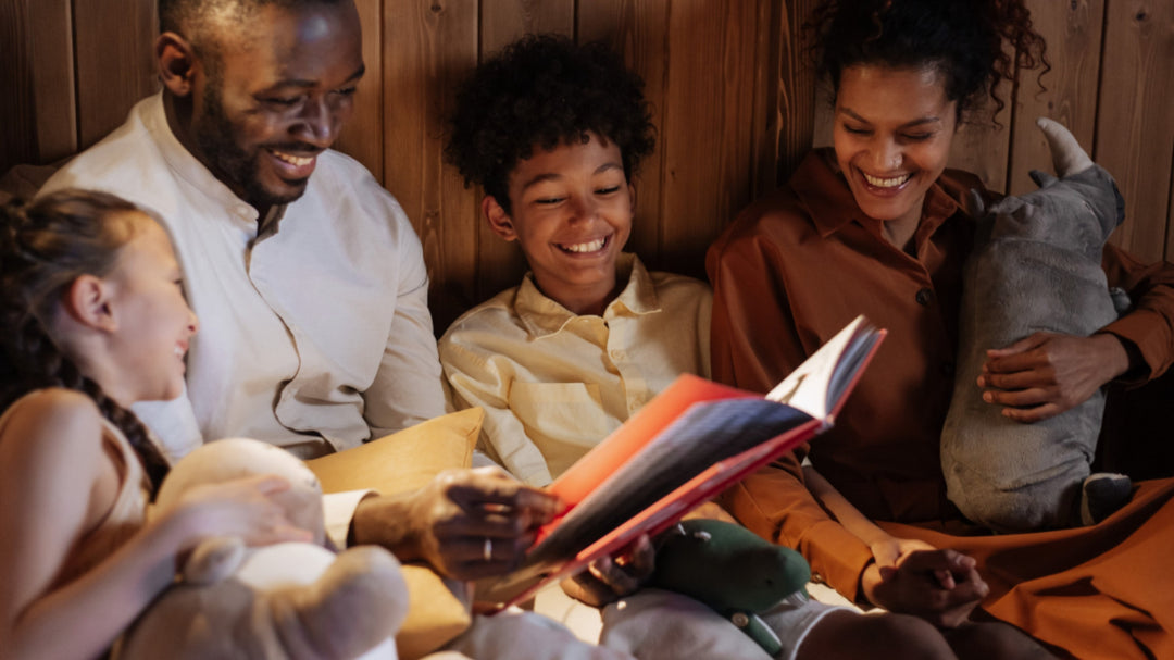A happy family, two adults and two children, smiles as they read a book together in bed at night.