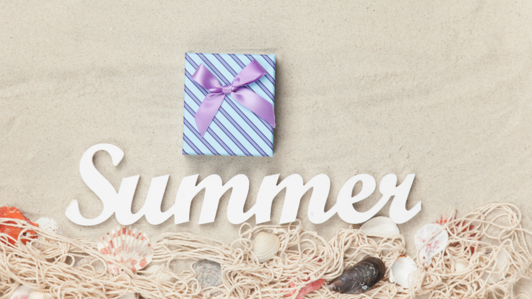 A purple gift box with a ribbon rests on sand with white “Summer” text and seashells below it.
