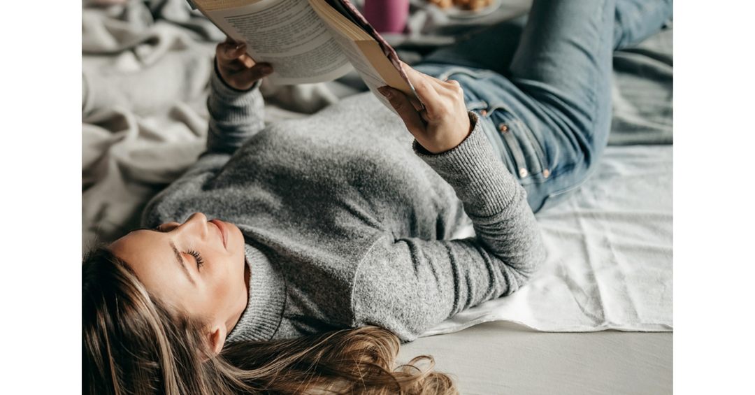 Person lying comfortably on a bed reading a book during a relaxing day indoors.