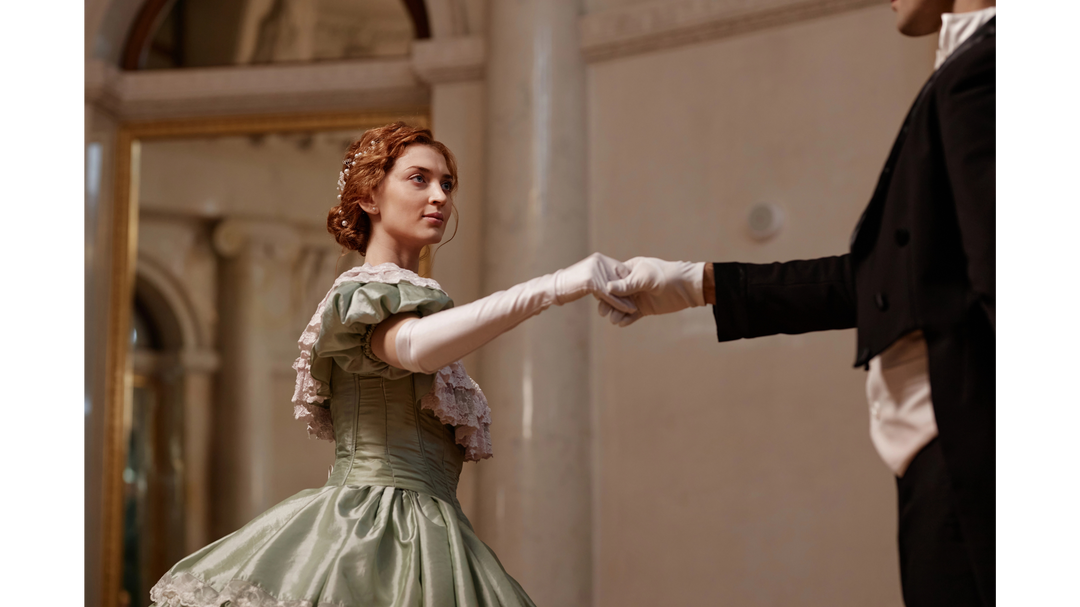 A grand ballroom scene with a woman in a Victorian gown dancing with a suited man, evoking historical romance.