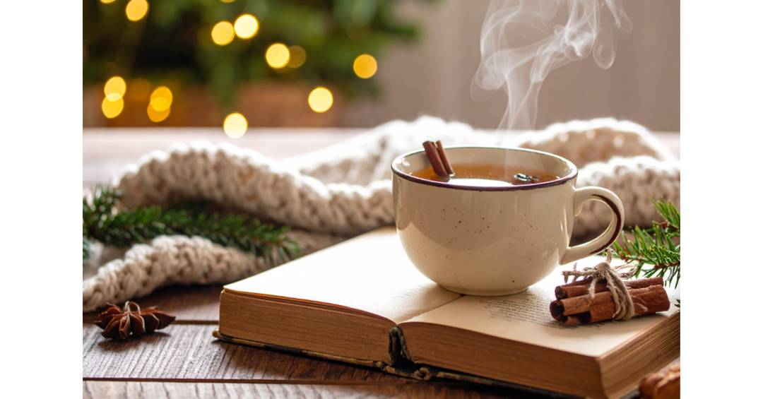 Cozy fall reading setup with an open book, steaming mug, warm blanket, cinnamon sticks, and soft lights.
