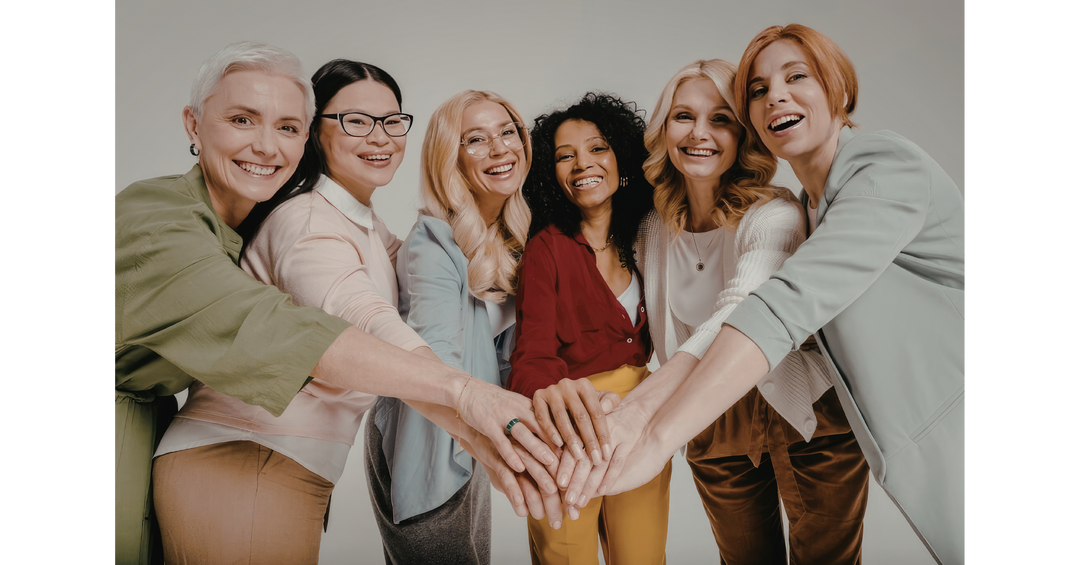 Diverse group of women smiling with their hands stacked together, celebrating friendship, unity, and women's empowerment.