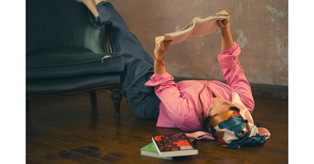 A person lying on the floor beside a chair, relaxing while reading a book indoors.