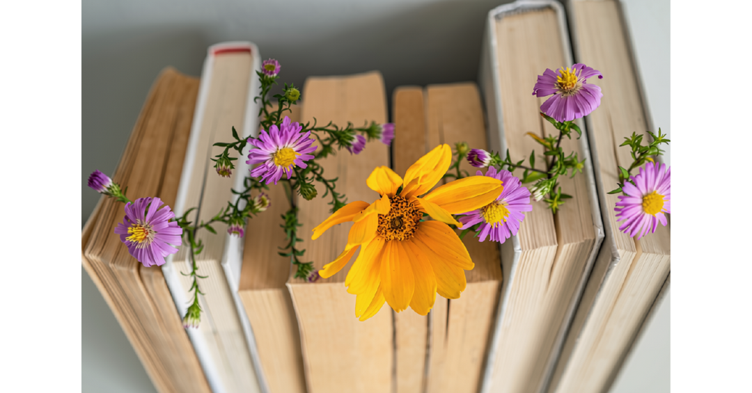 Colorful wildflowers resting between stacked books, creating a bright and cheerful bookish display.