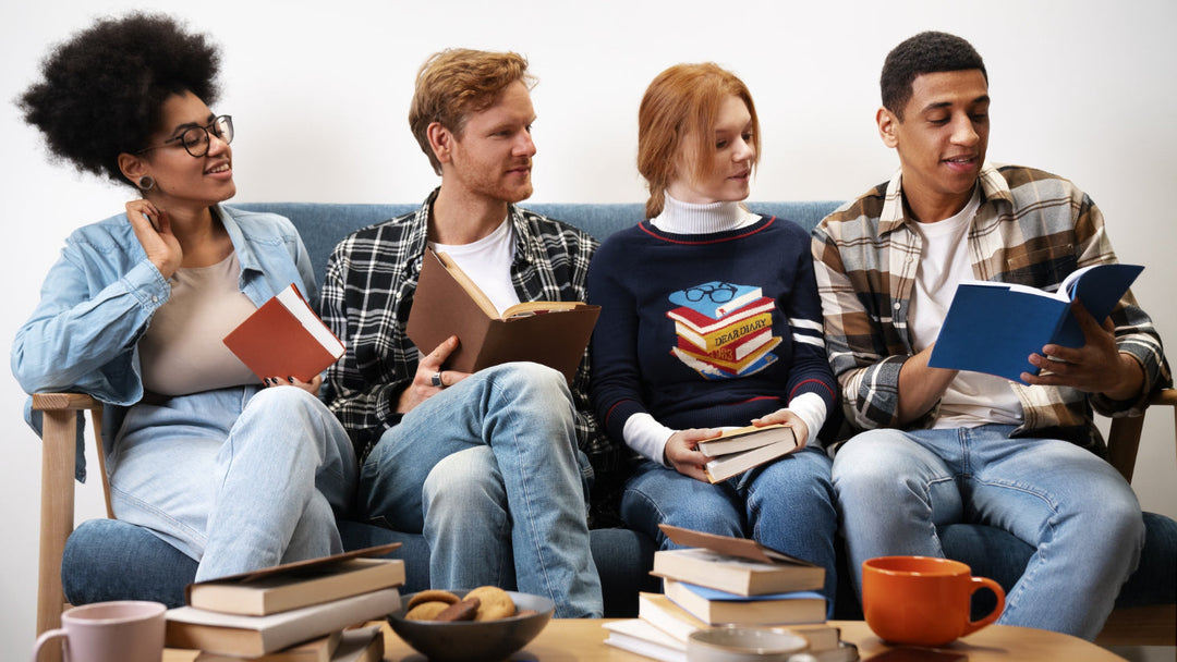 A group of four people sitting on a couch enjoying a book discussion, surrounded by books and mugs on a coffee table.