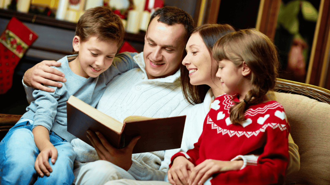 A happy family sits together reading a book, surrounded by cozy holiday decorations.
