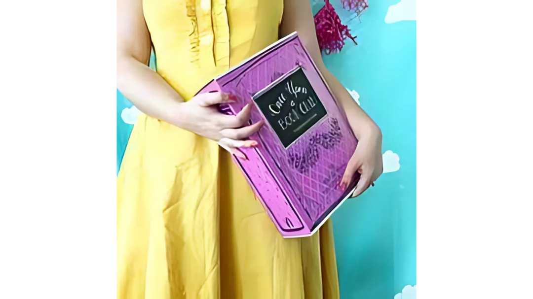 A person in a yellow dress holding a pink Once Upon a Book Club box against a teal background with white cloud shapes.