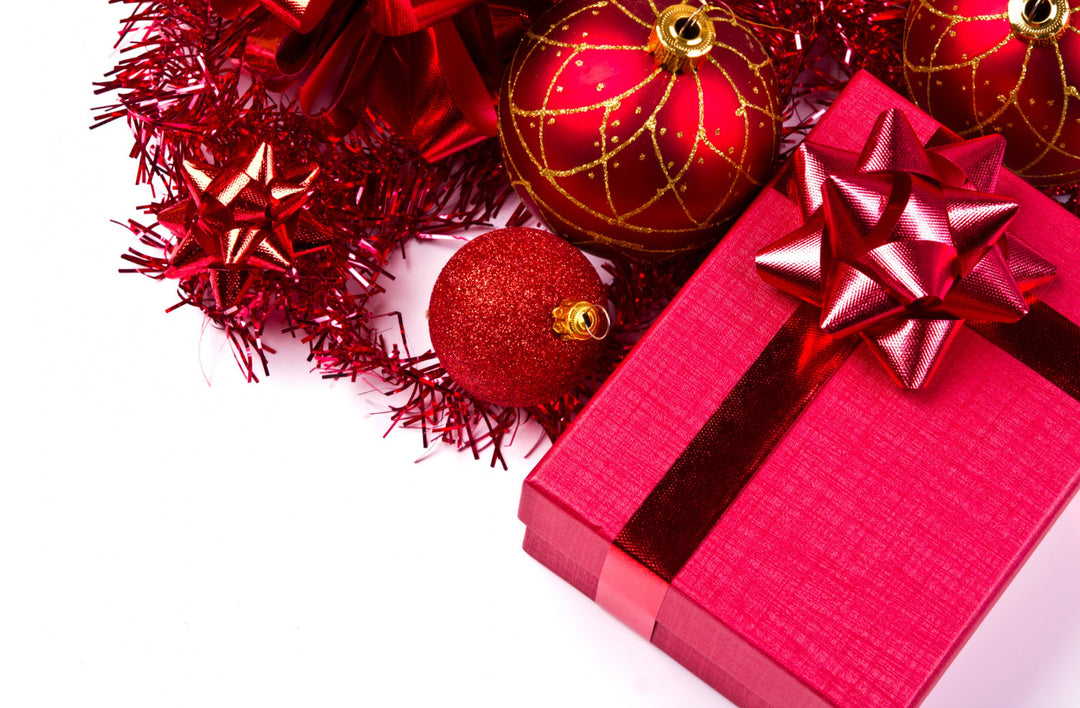 A festive arrangement featuring a red gift box with a bow, glittery ornaments, and red tinsel on a white background.