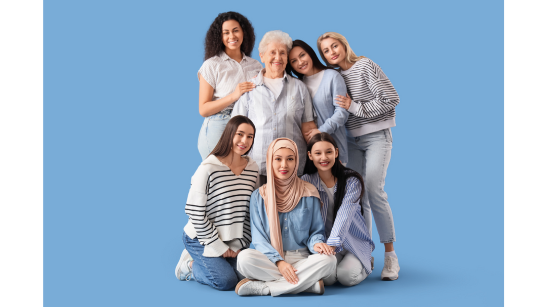 Multi-generational group of women standing and sitting together against a blue background, smiling and embracing.