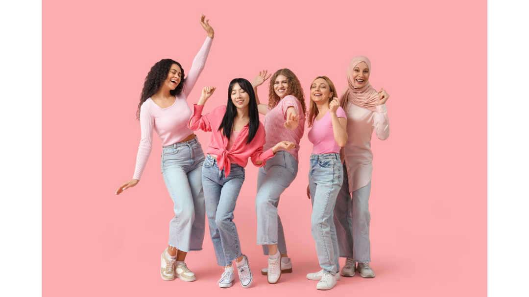 Diverse group of women dressed in pink outfits dancing together against a solid pink background.