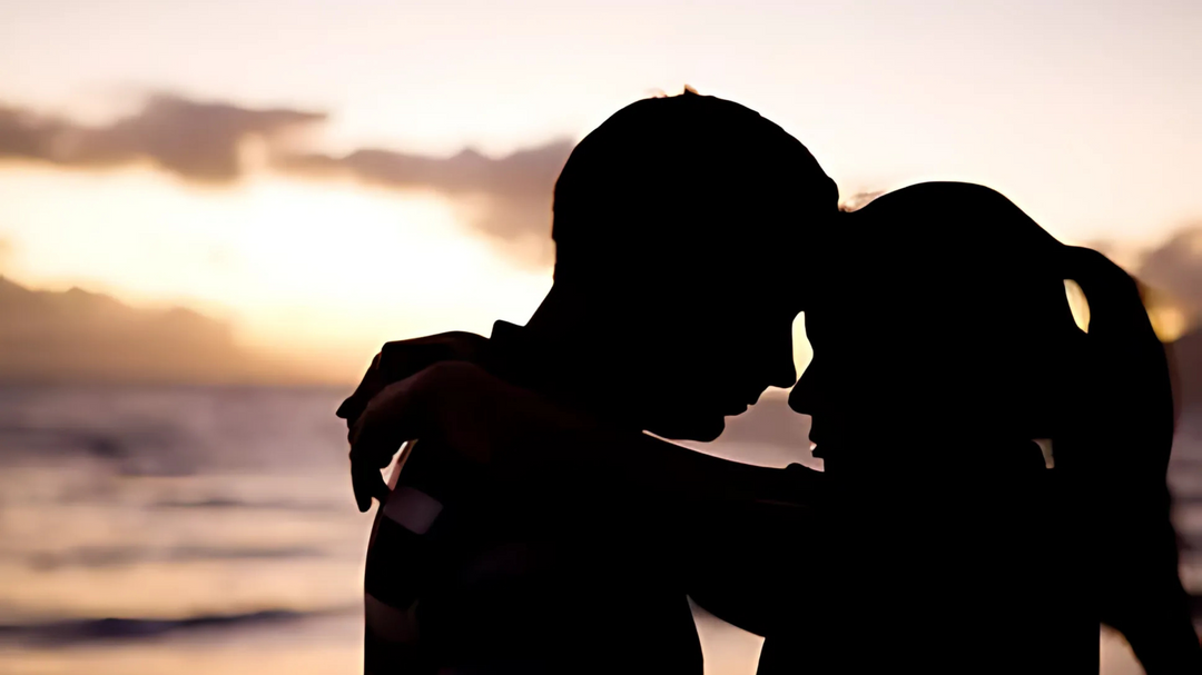 A couple embraces at sunset, their silhouettes softly blending into the golden hues of the ocean horizon, evoking warmth and intimacy.