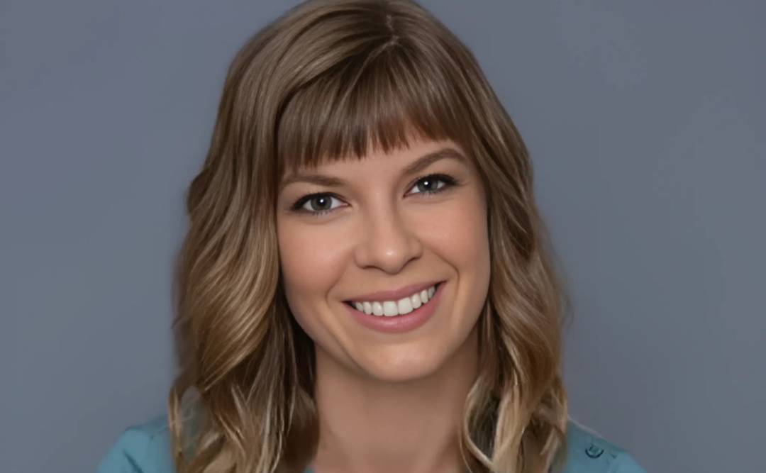 A portrait of author Jess Redman, smiling warmly with shoulder-length wavy hair and wearing a blue top, set against a neutral background.