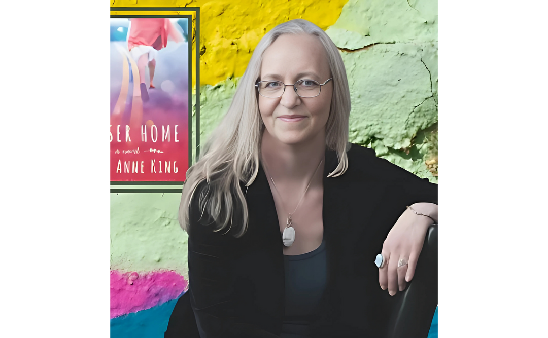 Portrait of Kerry Anne King, an author, sitting in front of a colorful background with her book cover "Whisper Me This" prominently displayed.