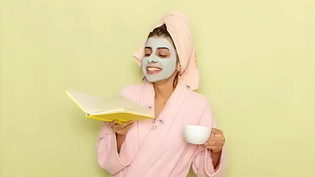 A woman wearing a pink robe and green face mask, holding a book in one hand and a cup in the other, against a light green background.