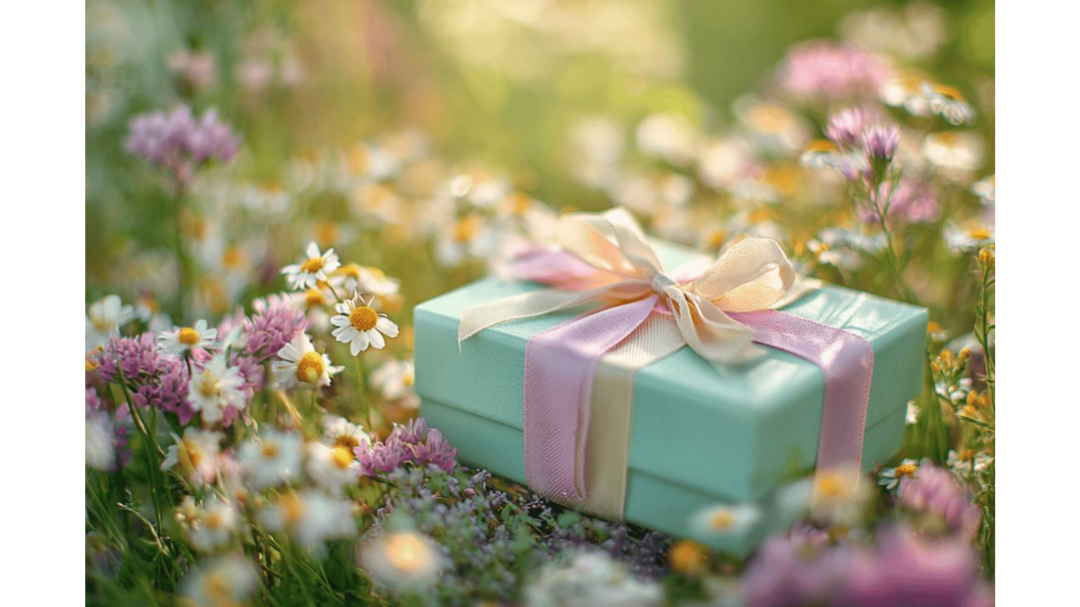 Mint green gift box with a pink ribbon placed in a sunlit field of wildflowers.