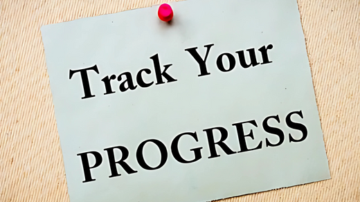 A beige note pinned to a corkboard with the words "Track Your Progress" written in bold black letters.