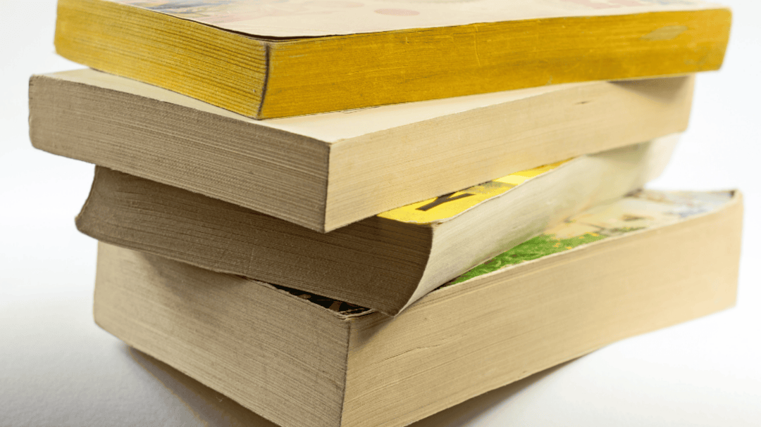 Stack of worn paperbacks with bent spines and yellowed pages sitting on a white background.