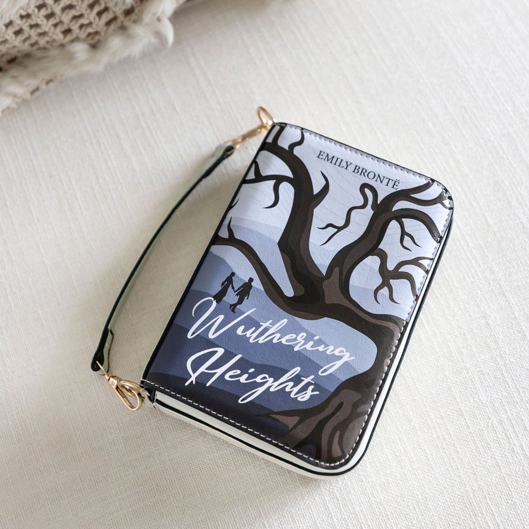 A zippered purse designed with a Wuthering Heights cover illustration, featuring a silhouetted tree and figures, resting on a light fabric surface.