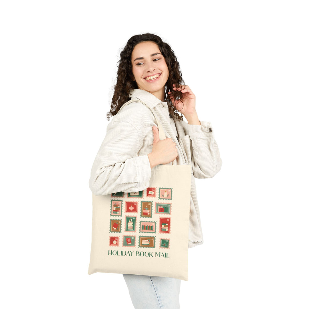 Woman holding a tote bag with 'Holiday Book Mail' stamp design on a white background