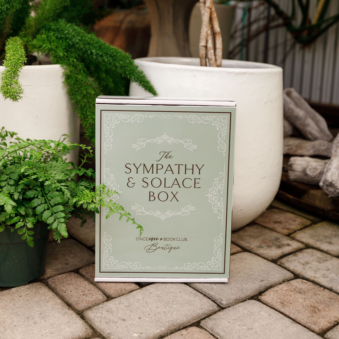 A sage green Sympathy & Solace box sits outdoors surrounded by greenery.