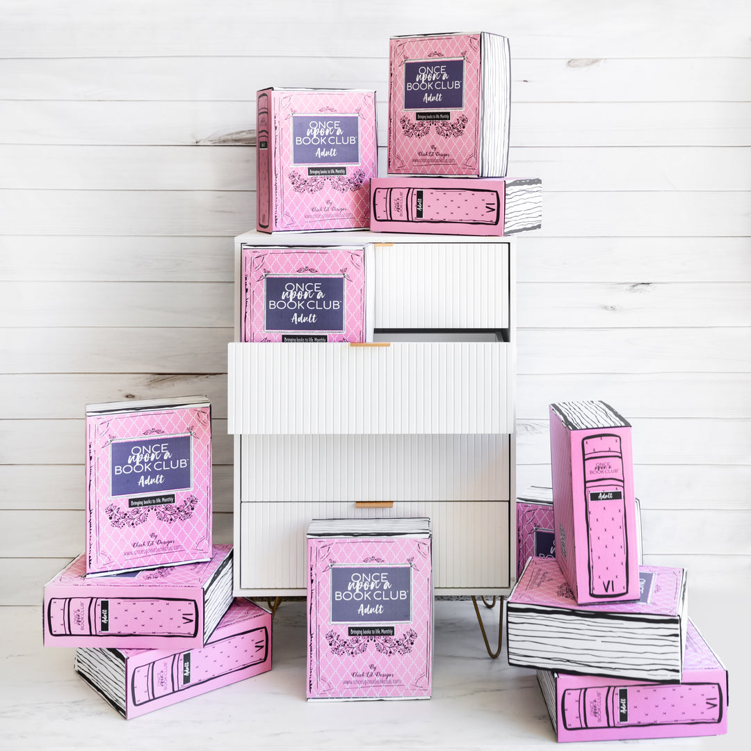 12 pink Once Upon a Book Club Adult boxes sit on and around a chest of drawers