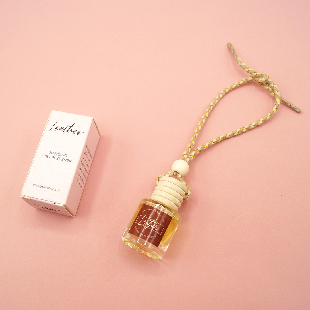 a bottle of leather scented air freshener in a hanging car diffuser and matching box on a pink background.