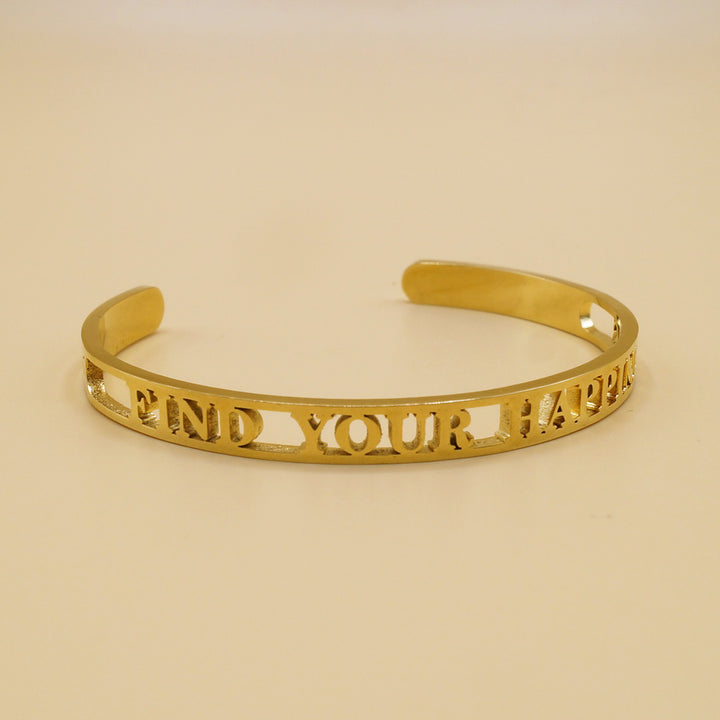 A gold bangle bracelet with the engraved words "FIND YOUR HAPPINESS" displayed against a simple light background.