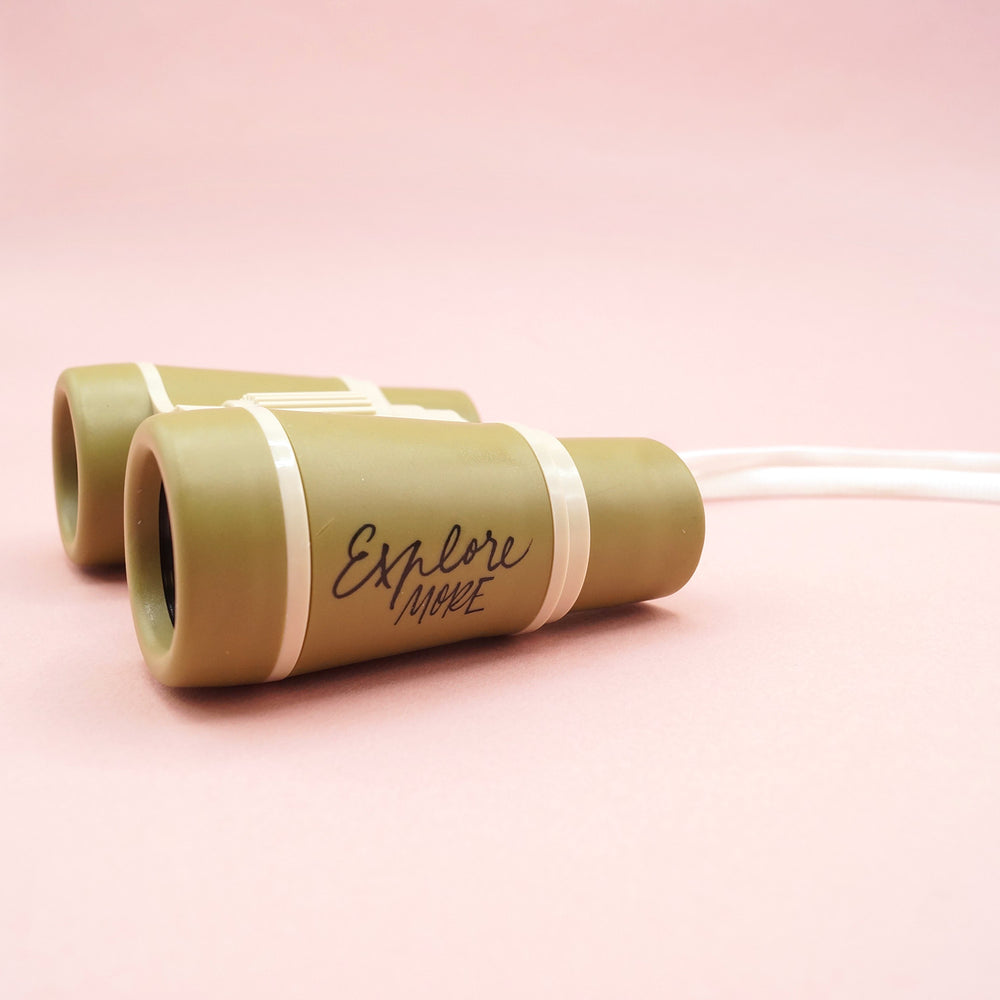 Green binoculars with 'Explore More' text  on the side of eyepiece on a pink background