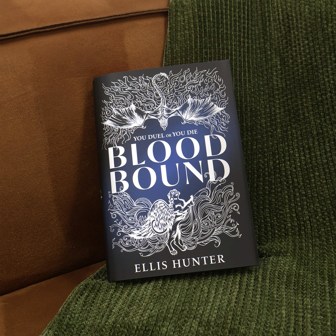 The book 'Blood Bound' by Ellis Hunter, featuring a reversible dark navy blue cover with white gothic illustrations and typography, resting on a textured green knit blanket next to a brown leather surface.
