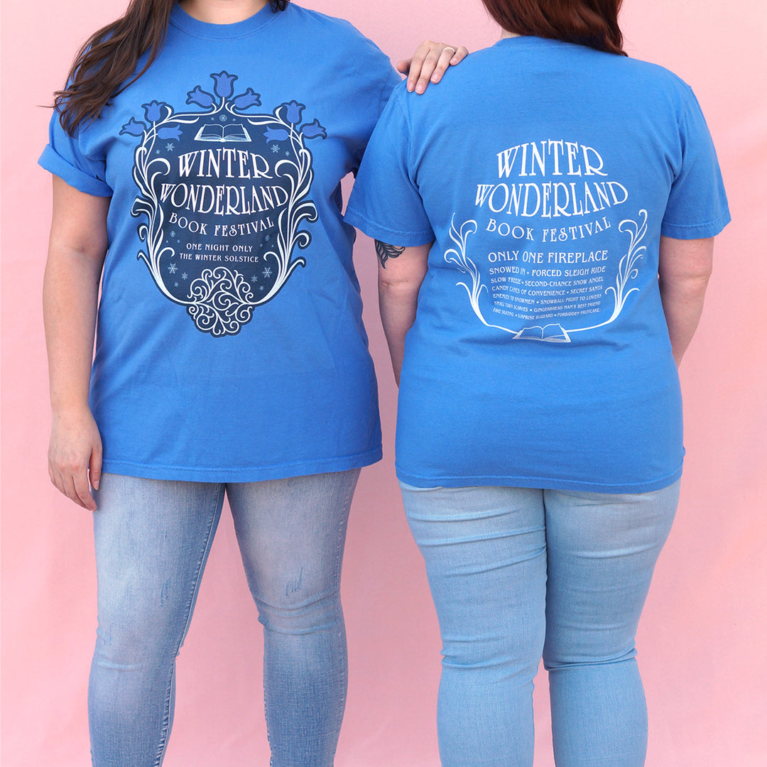 Two people wearing blue t-shirts with 'Winter Wonderland Book Festival' design on a pink background