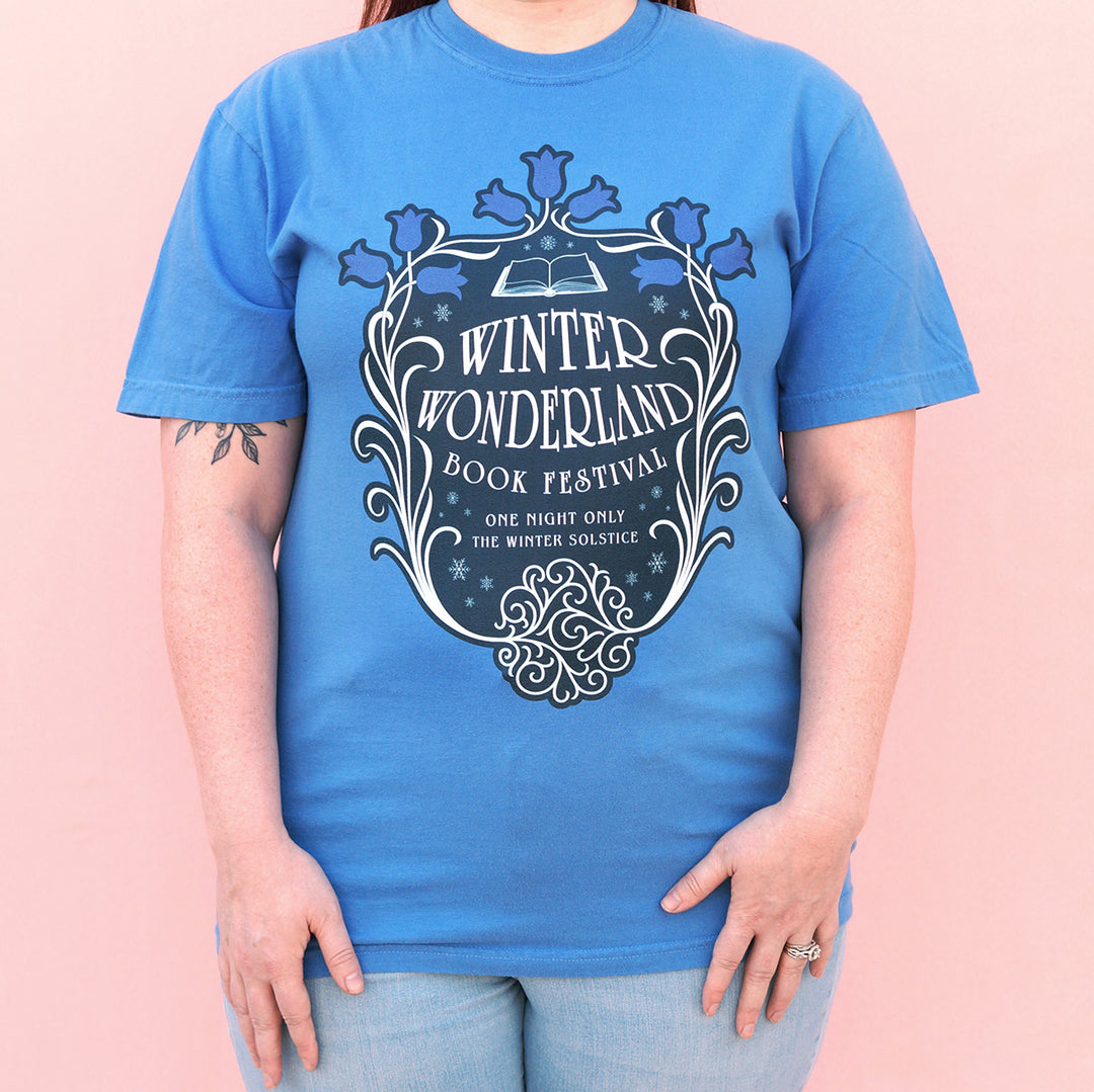Person wearing a blue t-shirt with 'Winter Wonderland Book Festival' design on a pink background