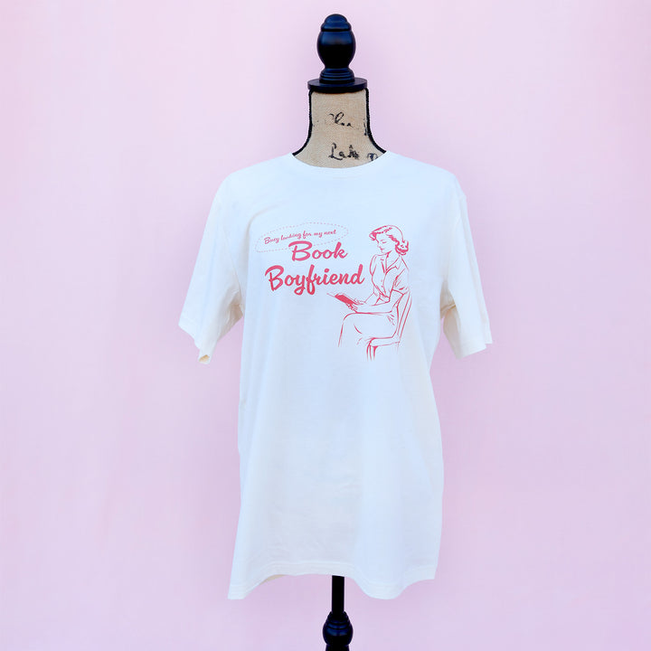 White t-shirt with red text and graphic on a mannequin against a pink background