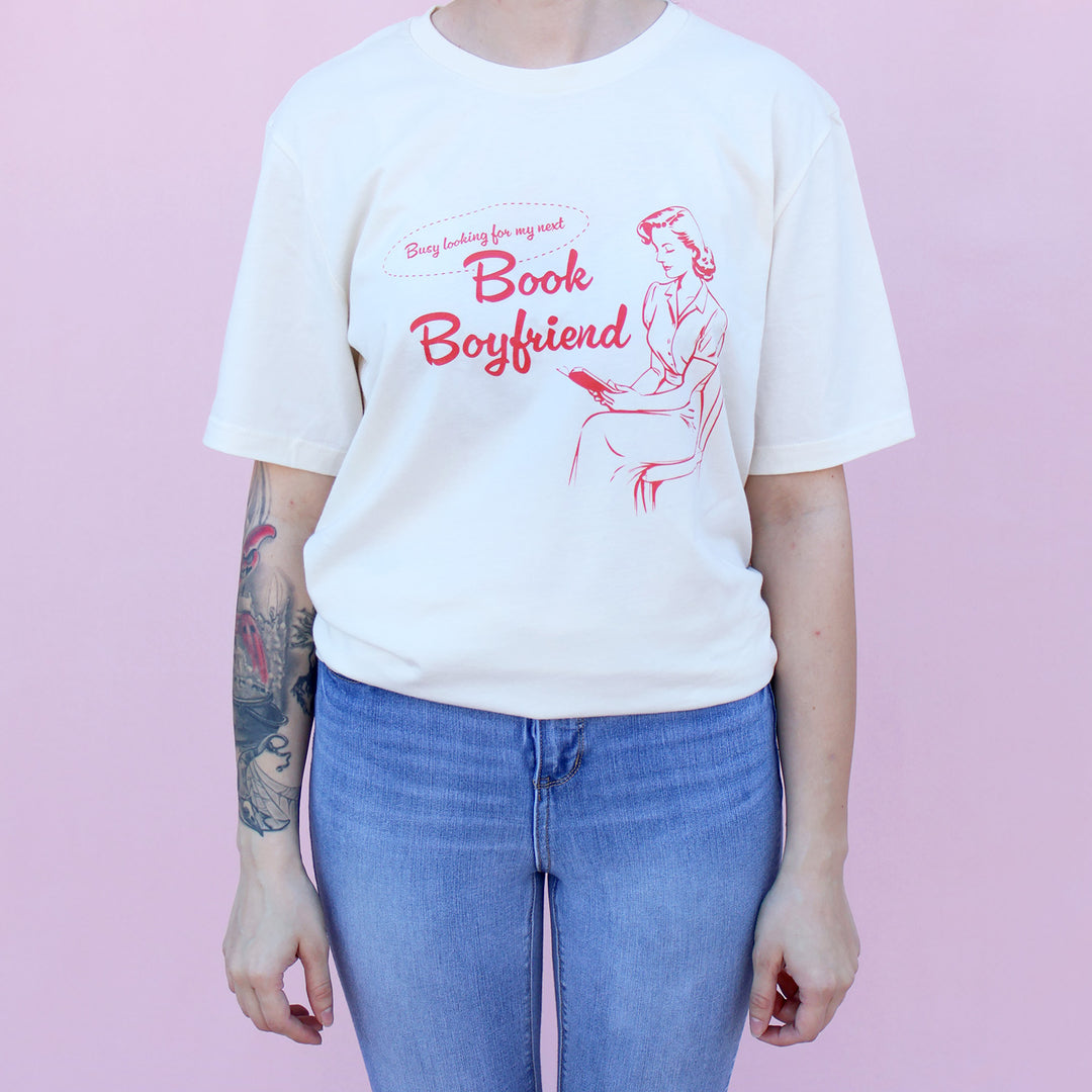 Person wearing a white t-shirt with red text and graphic on a pink background