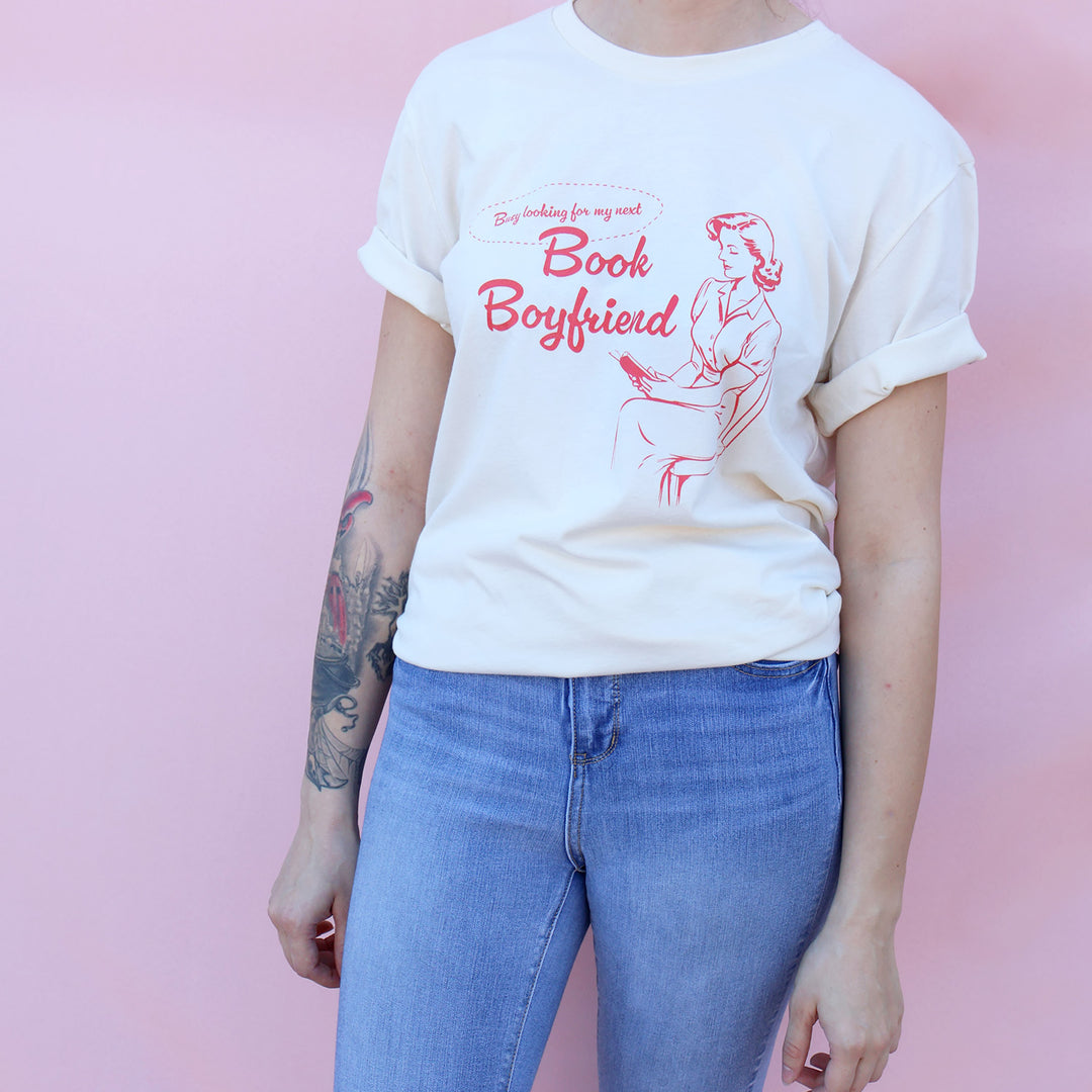Person wearing a white t-shirt with red text and graphic on a pink background