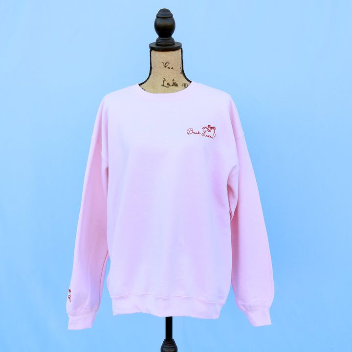 Pink sweatshirt with a red embroidered book lover quote and bow on a mannequin against a blue background