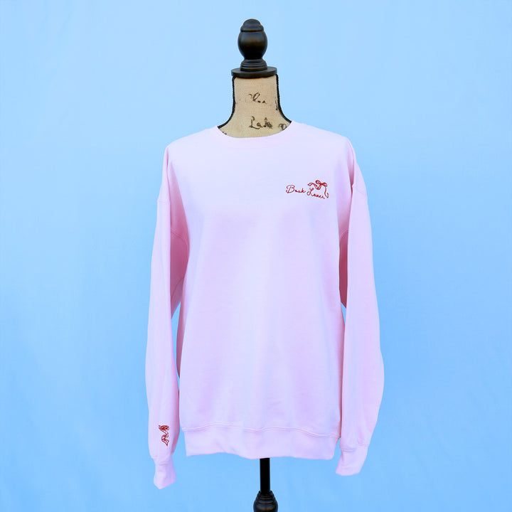 Pink sweatshirt with a red embroidered book lover quote and bow on a mannequin against a blue background