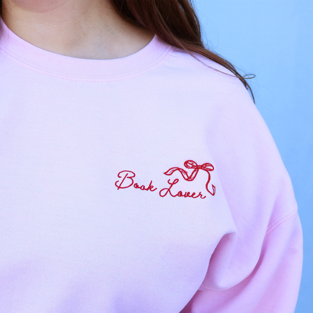 Pink sweatshirt with 'Book Lover' embroidery on a light blue background