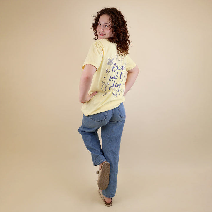 A woman wearing yellow t-shirts with 'Booked & Busy' on the front and 'Ask Me What I'm Reading' on the back surrounded by book-themed doodles.