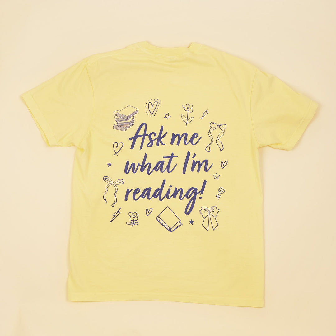 A yellow t-shirt with 'Booked & Busy' on the front and 'Ask Me What I'm Reading' on the back surrounded by book-themed doodles.