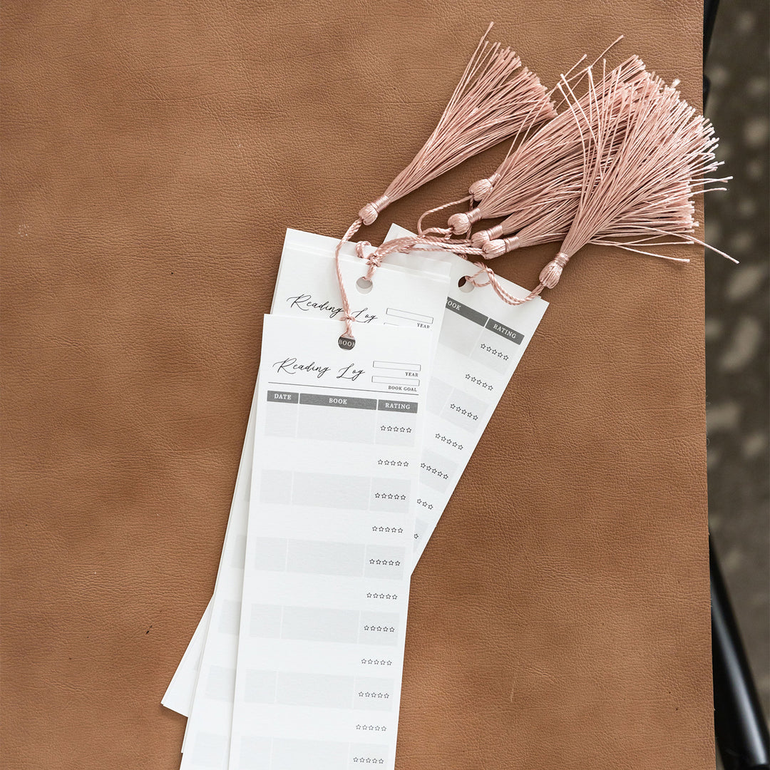 A stack of Reading Log bookmarks sits on a warm brown leather background.