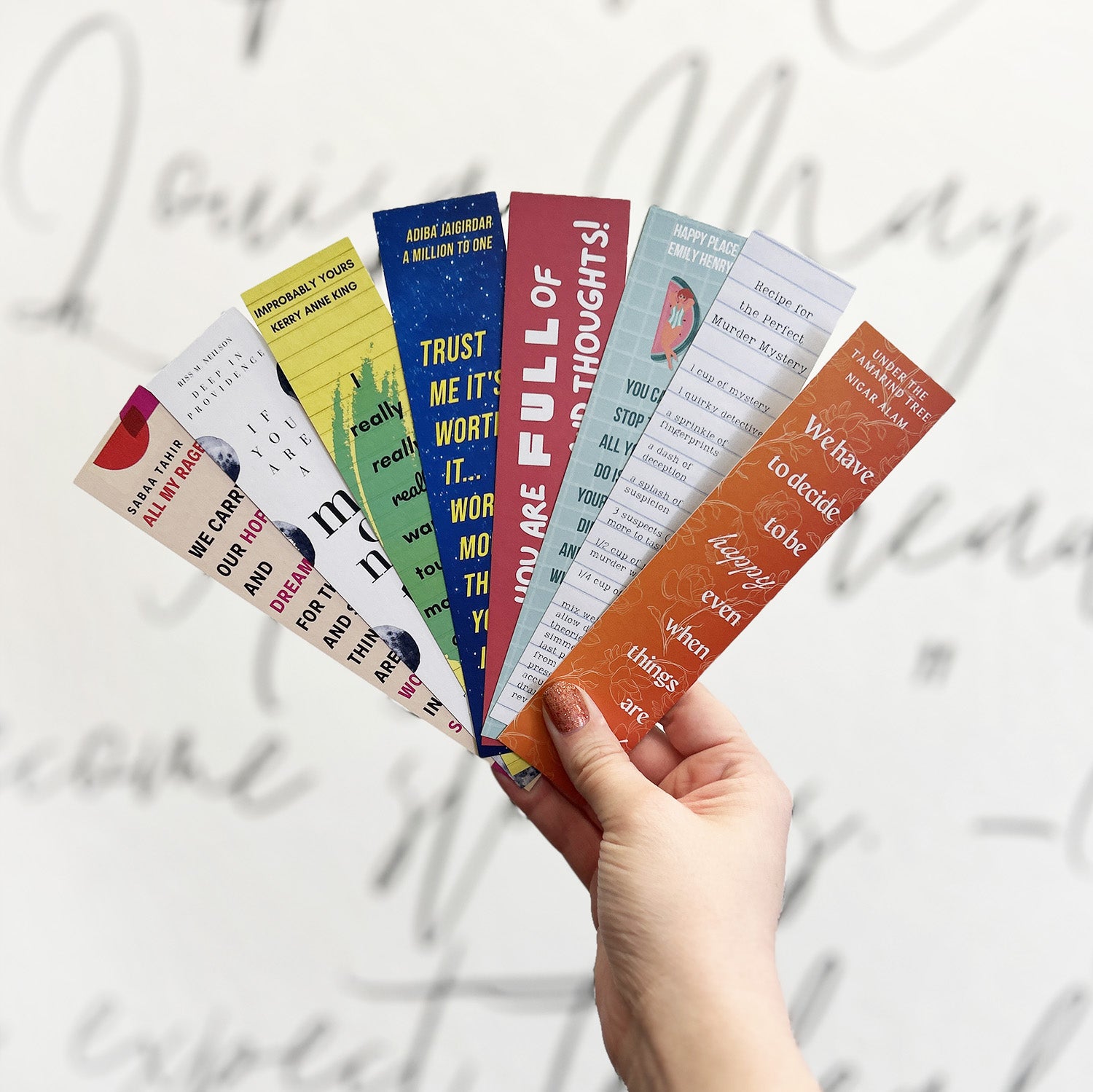 a white hand fans out 7 bookmarks in front of a white wall