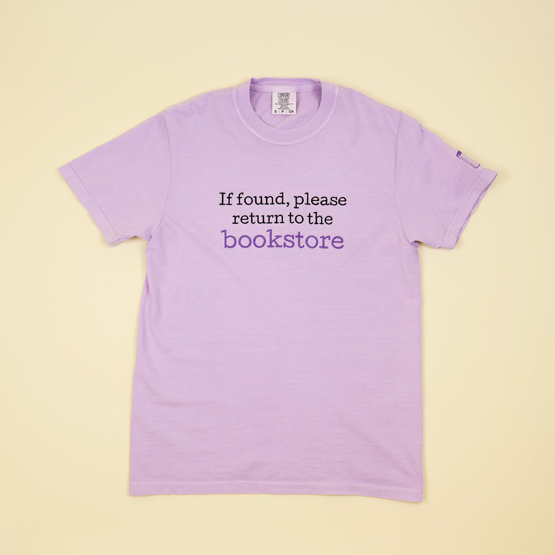 Purple t-shirt with text 'If found, please return to the bookstore' on a beige background