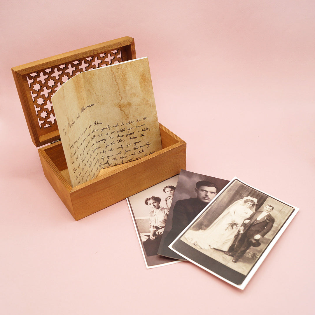 An open wooden box with a note sticking out of it and three black and white old photos next to it