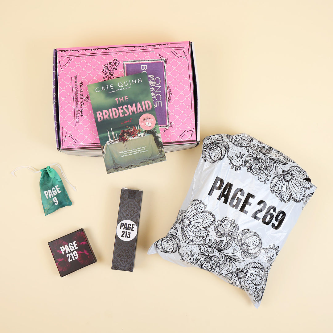 A paperback edition of The Bridesmaid stands on a pink OUABC box next to a small box labeled with a page number. In front of the box are three wrapped gifts labeled with page numbers.