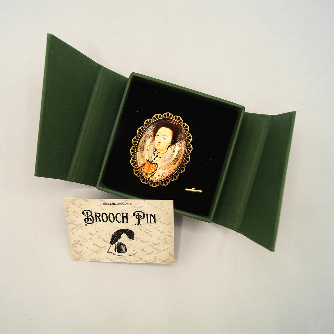 A gold brooch in an open green box with a woman's photo in the center. Labeled Brooch Pin