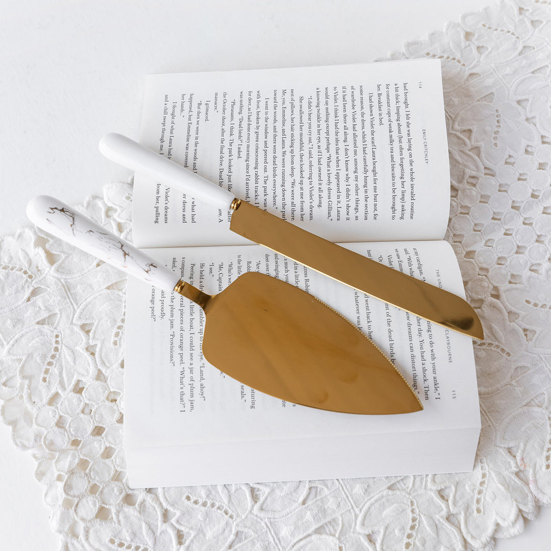 A gold cake serving set with white marble handles laying on an open book 